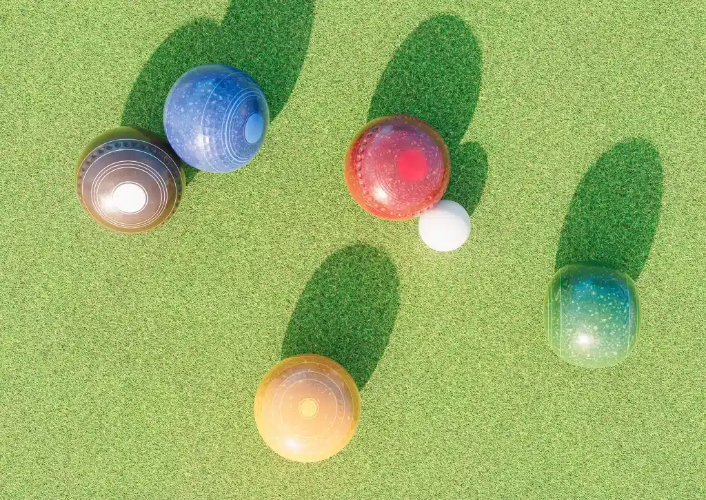 Top-down view of colorful bocce balls on a green lawn, with long shadows crossing the grass.